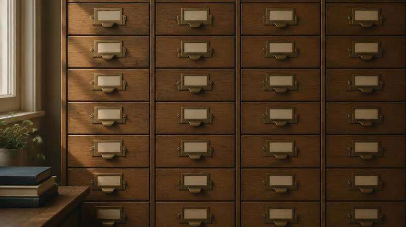 A wall of narrow wooden archive drawers with brass label holders